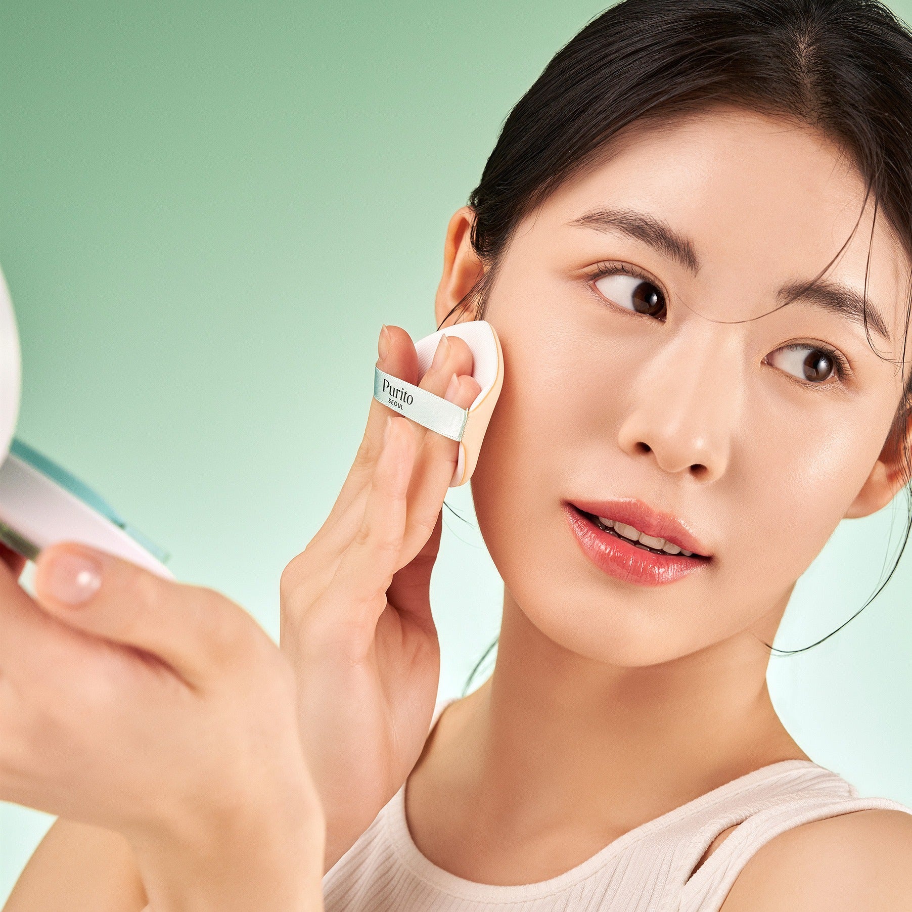PURITO Wonder Releaf Celtella BB Cushion 15g de Purito, femme maquillage appliquant le BB en studio sur fond vert.