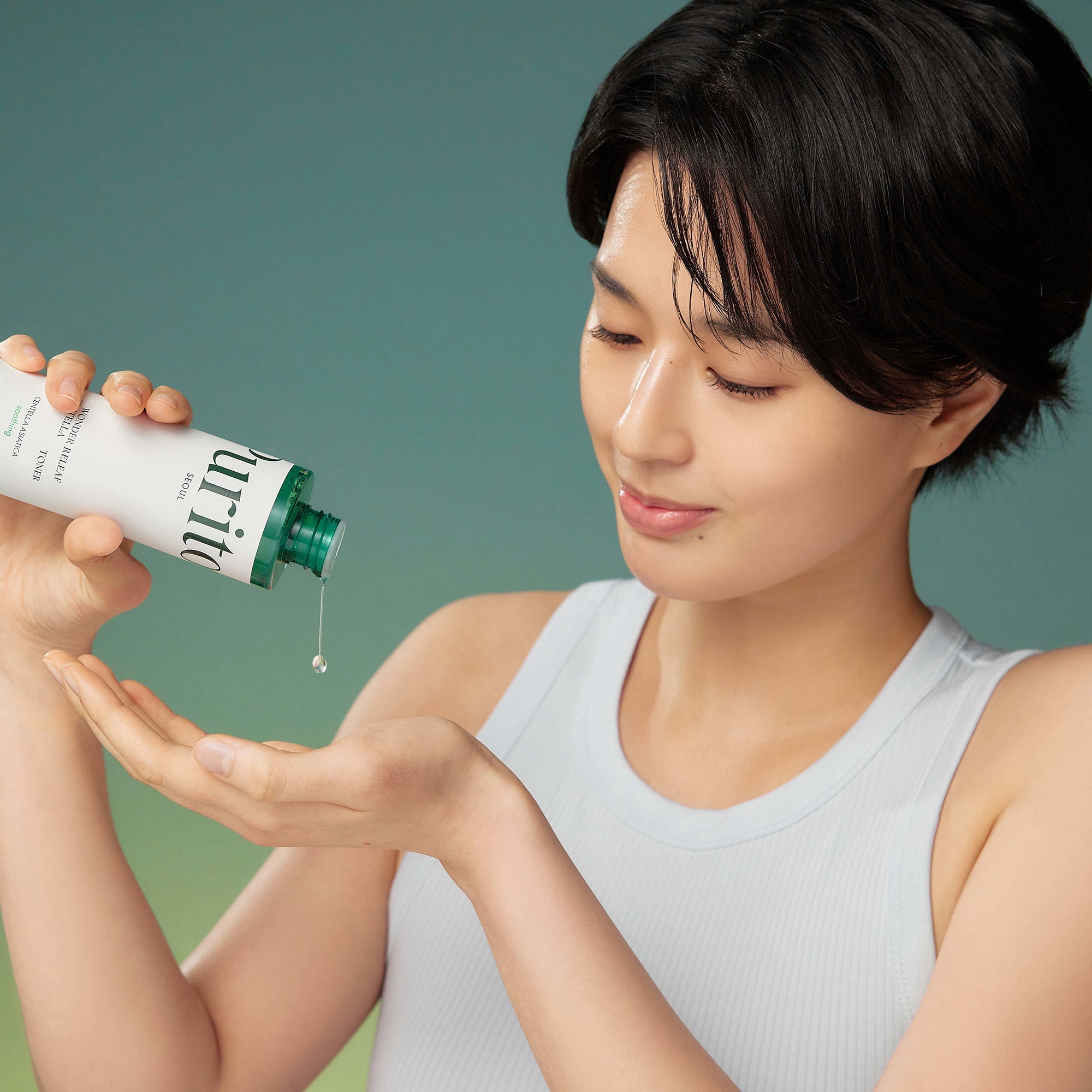 PURITO Wonder Releaf Centella Toner 200ml : jeune femme applique le sérum; marque PURITO, flacon et goutte verte, fond vert.