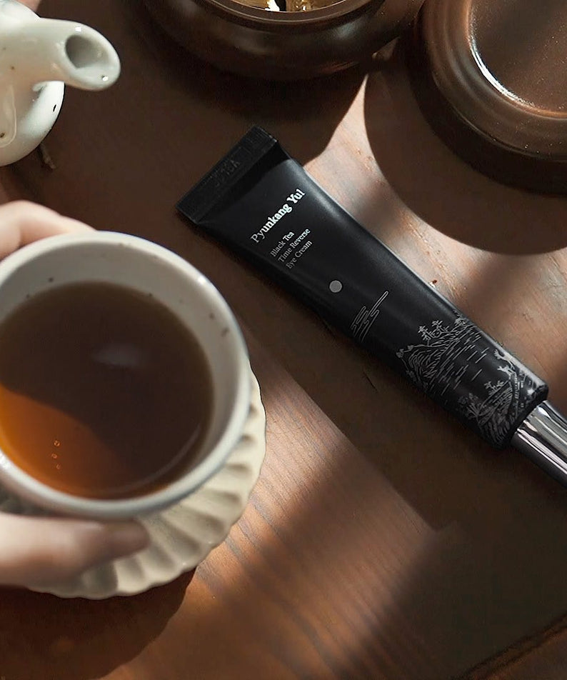 PYUNKANG YUL Black Tea Time Reverse Eye Cream 25ml de la marque, en mise en scène sur table avec tasse de thé noir.