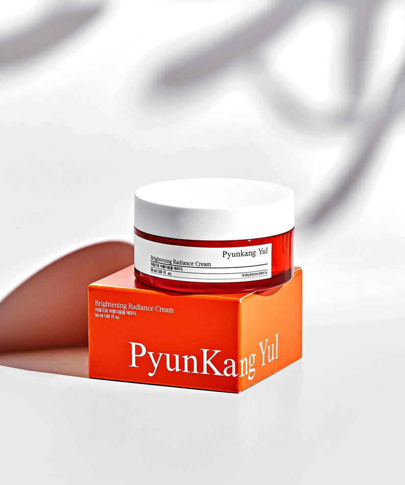 Crème "PYUNKANG YUL Brightening Radiance Cream 50ml" posée sur une boîte, lumière et ombres en arrière-plan.
