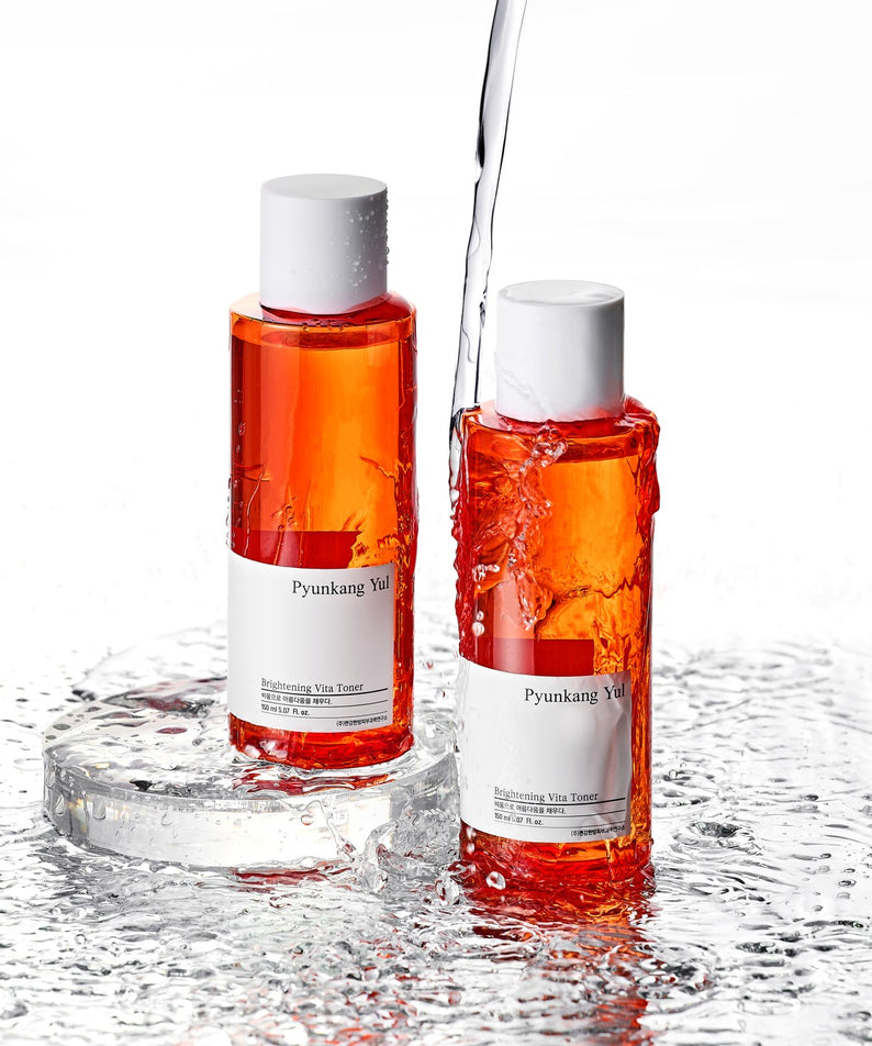 Deux bouteilles de PYUNKANG YUL Brightening Vita Toner 150ml sur fond mouillé, montrant une formule éclaircissante et hydratante.