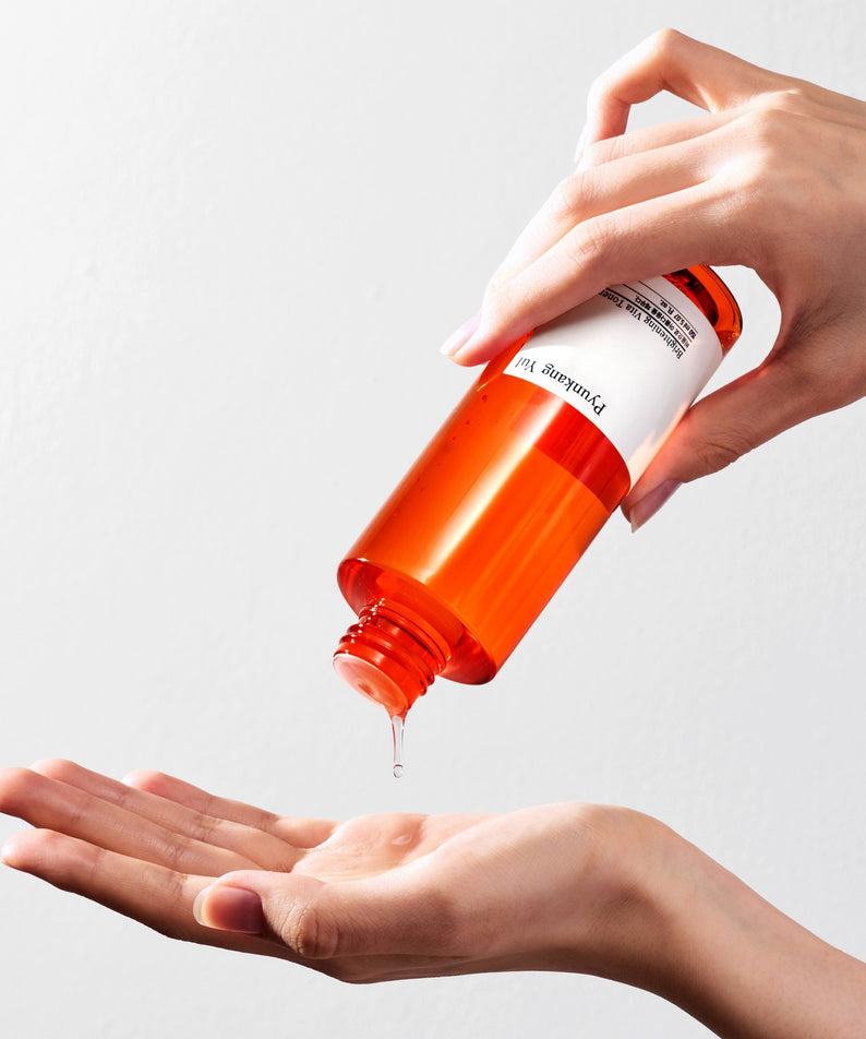 Application du toner PYUNKANG YUL Brightening Vita Toner 150ml sur la main, bouteille orange, soin du visage lumineux.