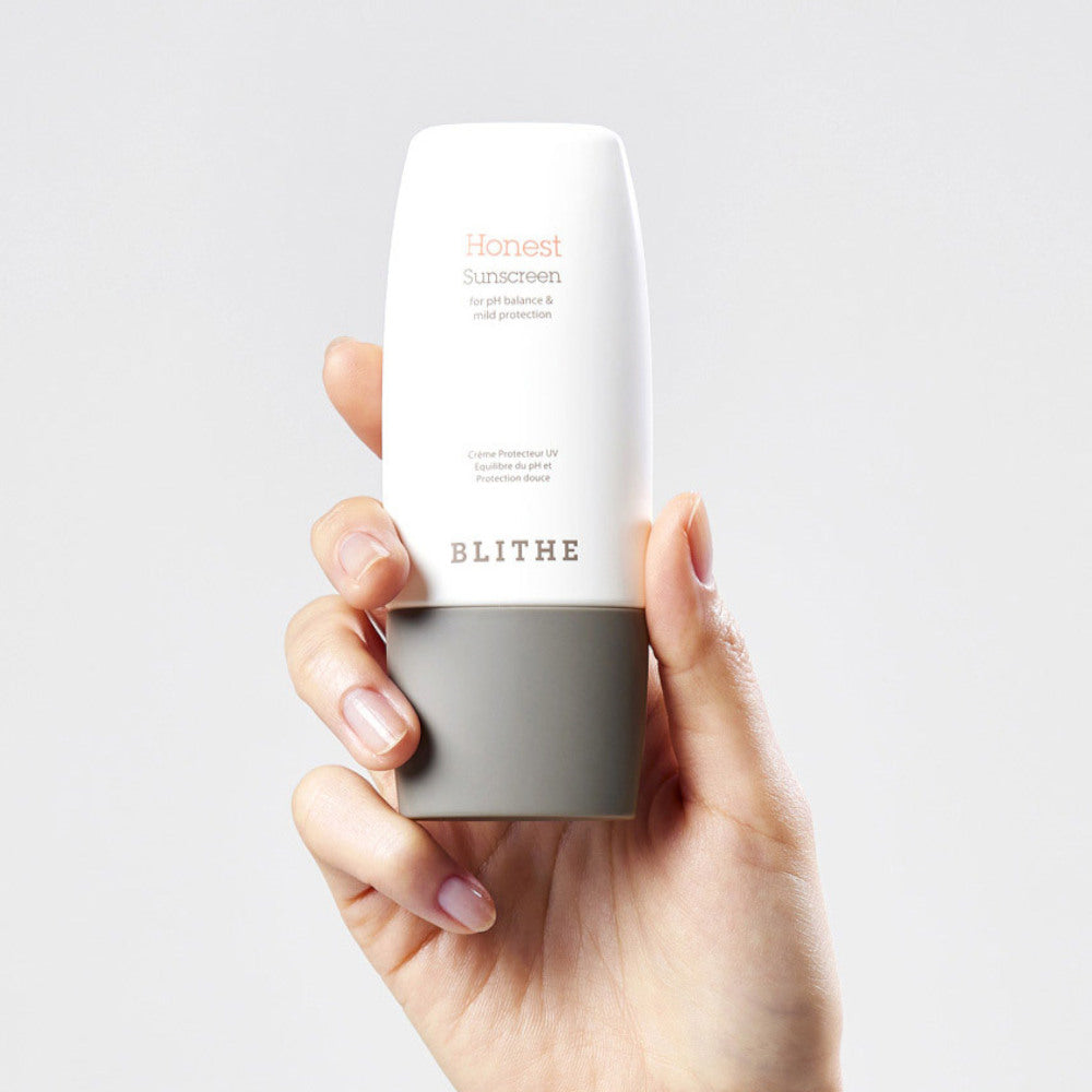 Main tenant BLITHE Honest Sunscreen 50ml, crème solaire blanche, fond clair minimaliste, marque BLITHE visible.