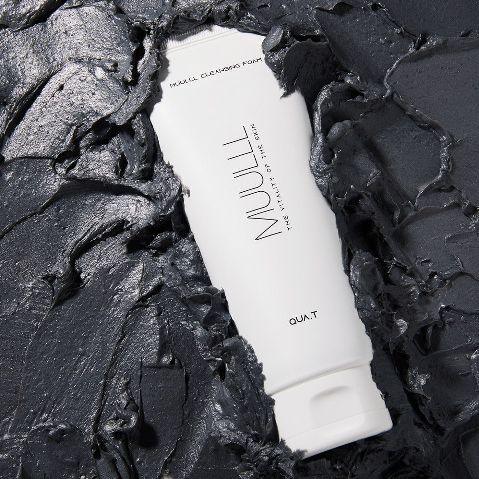 QUA-T Cleansing foam 150g de QUA.T, tube blanc sur fond noir texturé, mise en scène produit.