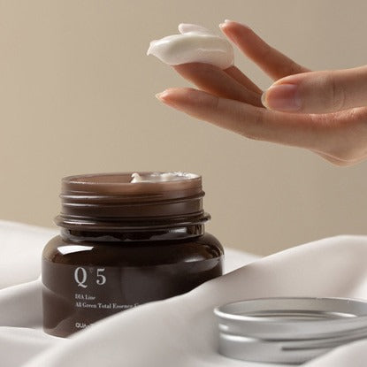 QUA-T Dia All Green Total Essence Cream 100ml de QUA-T, crème verte en pot, main appliquant, contexte soin visage.