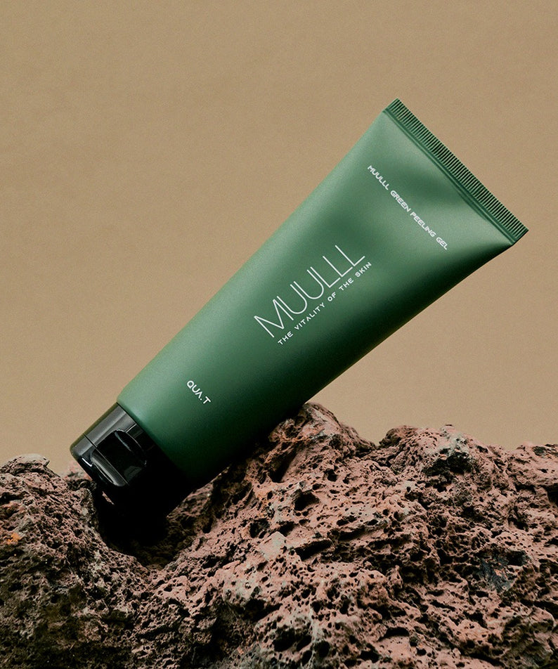 QUA-T Green Peeling Gel 150ml de la marque QUA-T, tube vert sur fond sable et roches, photo produit en studio.