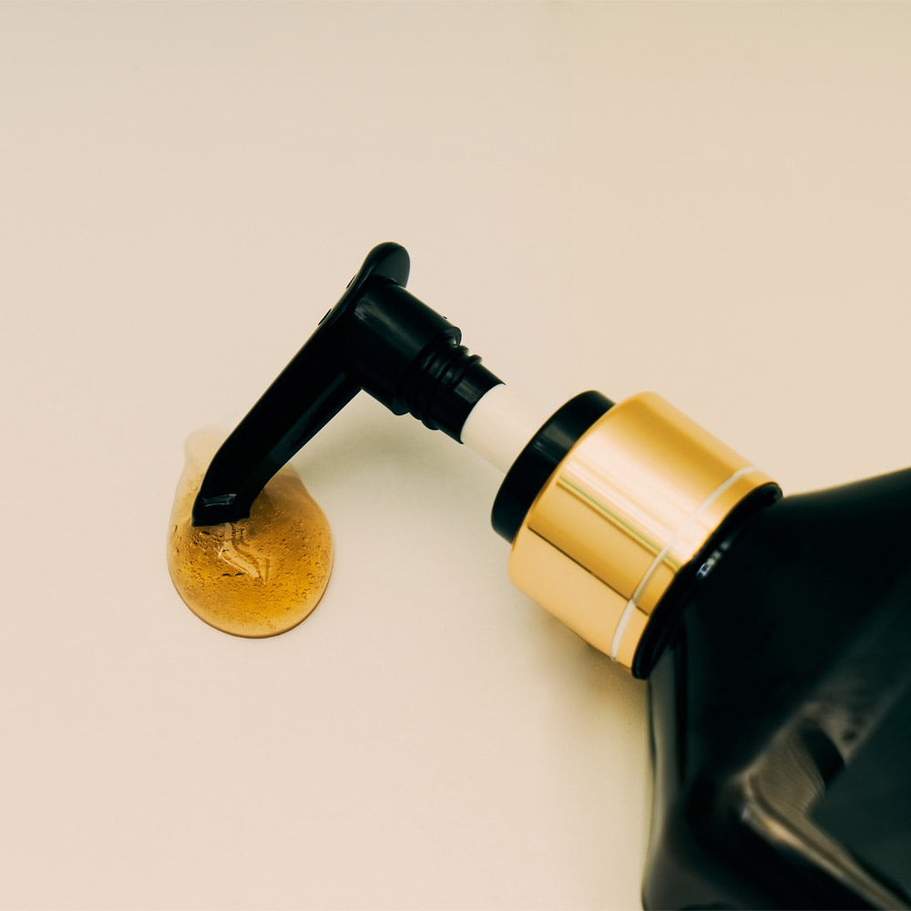 QUA-T Samjin Out Oil 220ml de Samjin, flacon noir et or sur fond clair, goutte d’huile visible.