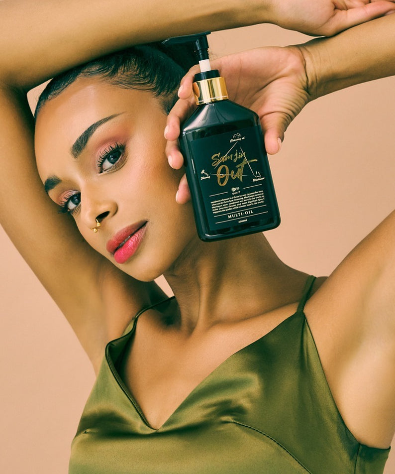 QUA-T Samjin Out Oil 220ml Samjin, flacon vert tenu par des mains sur une femme en pose spa, fond beige.