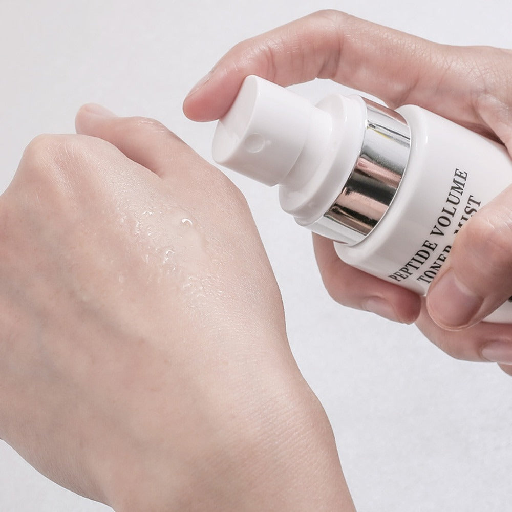 R828 Peptide Volume Toner Mist en main, pulvérisé sur la peau, image produit sur fond clair, soin visage.
