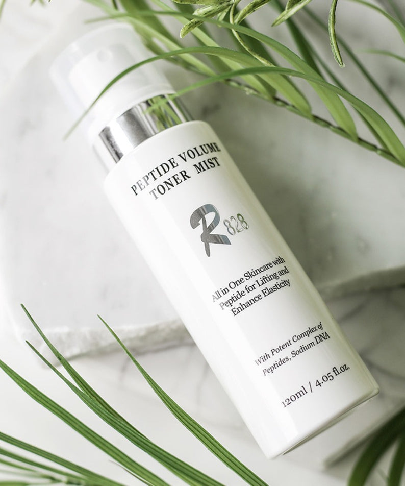 R828 Peptide Volume Toner Mist sur une table avec des feuilles vertes, un produit de soin pour la peau en flacon de 120ml.