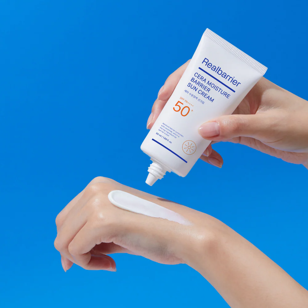 REAL BARRIER Cera Moisture Barrier Sun Cream 50ml, main appliquant une crème solaire sur peau, fond bleu.