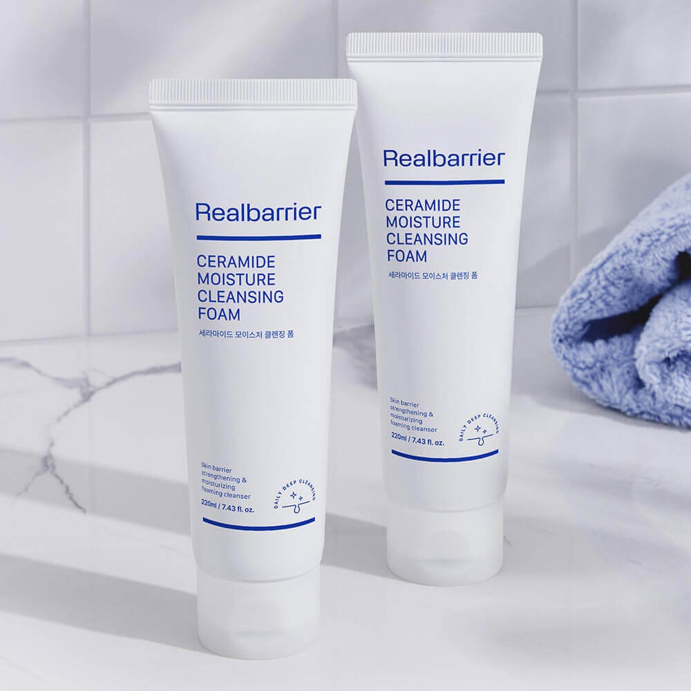 REAL BARRIER Ceramide Moisture Cleansing Foam 220ml Realbarrier, tubes blancs sur fond salle de bain avec serviette bleue.