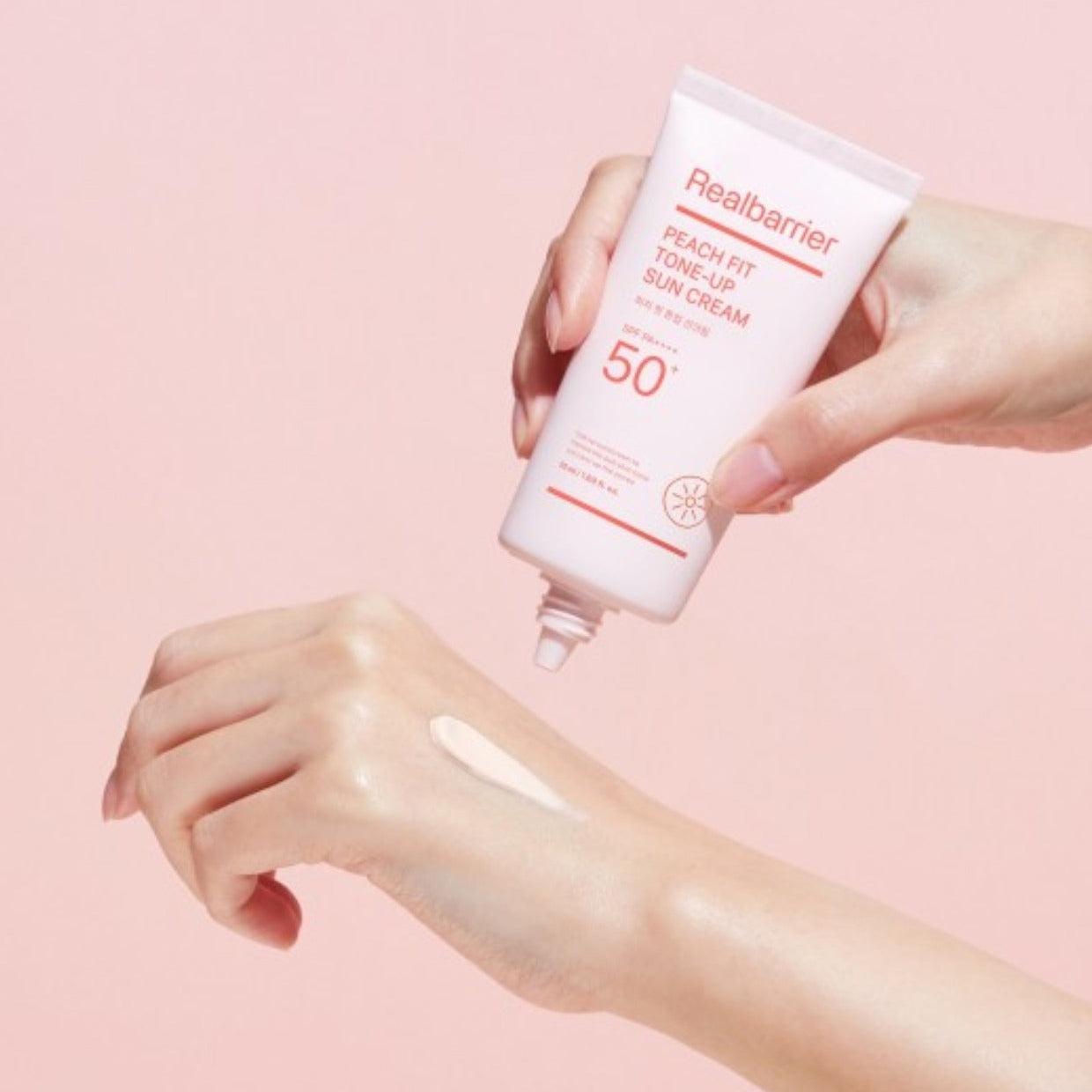 REAL BARRIER Peach Fit Tone-Up Sun Cream 50ml, crème solaire en tube, mains appliquant sur peau, fond rose, marque Real Barrier