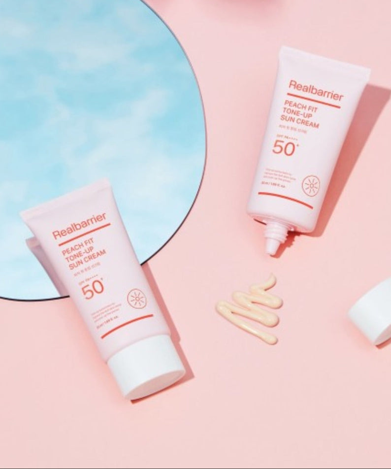 REAL BARRIER Peach Fit Tone-Up Sun Cream 50ml de marque Realbarrier, tubes solaires sur fond rose pastel, contexte beauté.