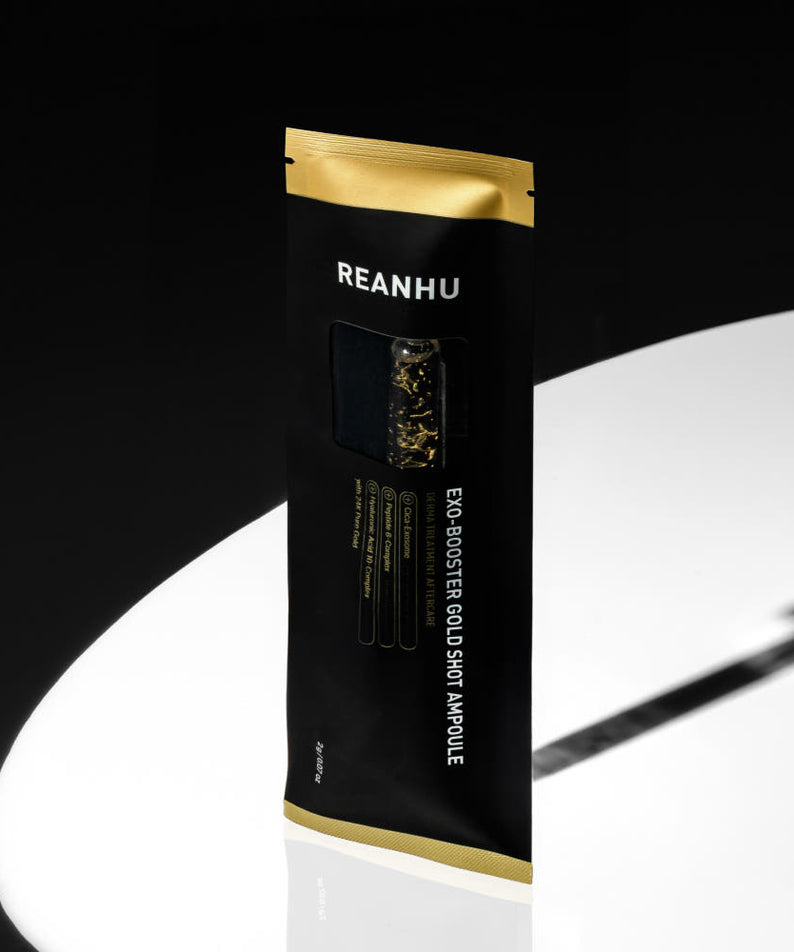 REANHU Exo Booster Gold Shot Ampoule 2 g X 7 ea, sachet noir et or REANHU sur fond clair, gouttelettes dorées visibles.