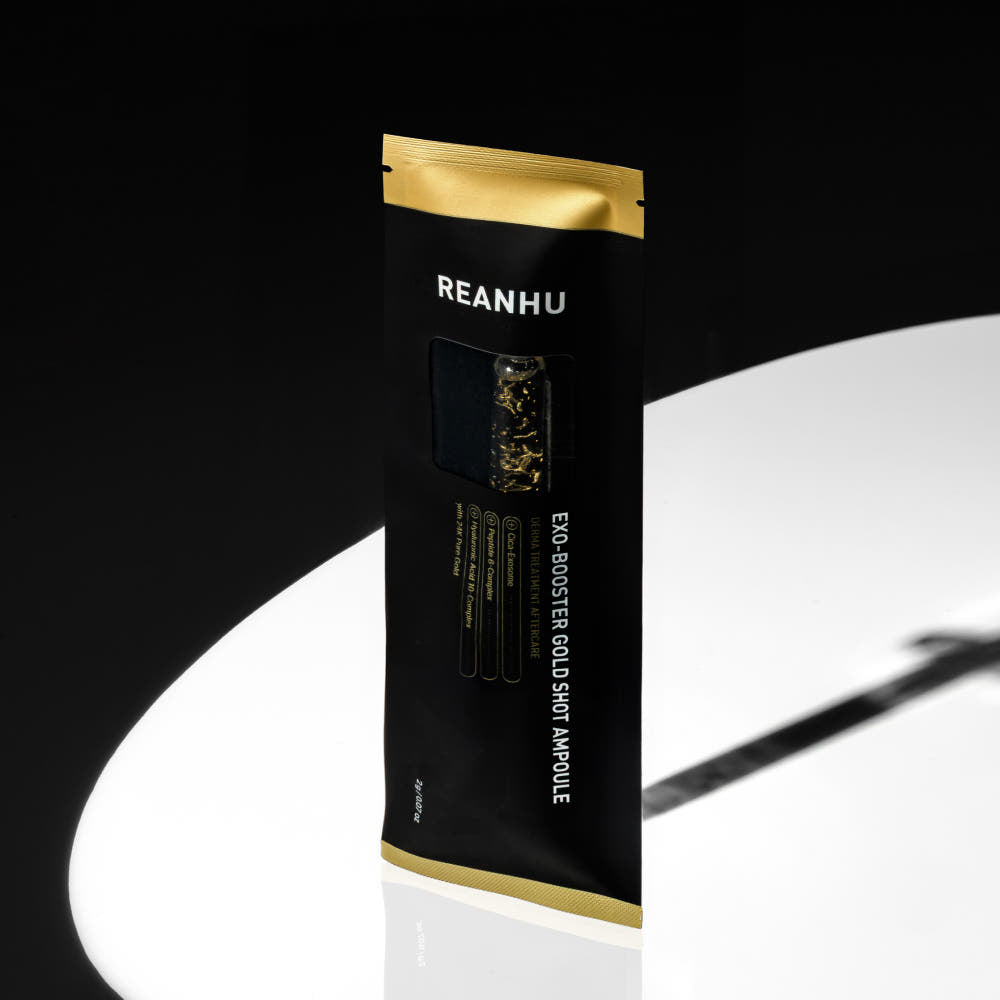 REANHU Exo Booster Gold Shot Ampoule 2 g X 7 ea, sachet noir et or REANHU sur fond clair, gouttelettes dorées visibles.