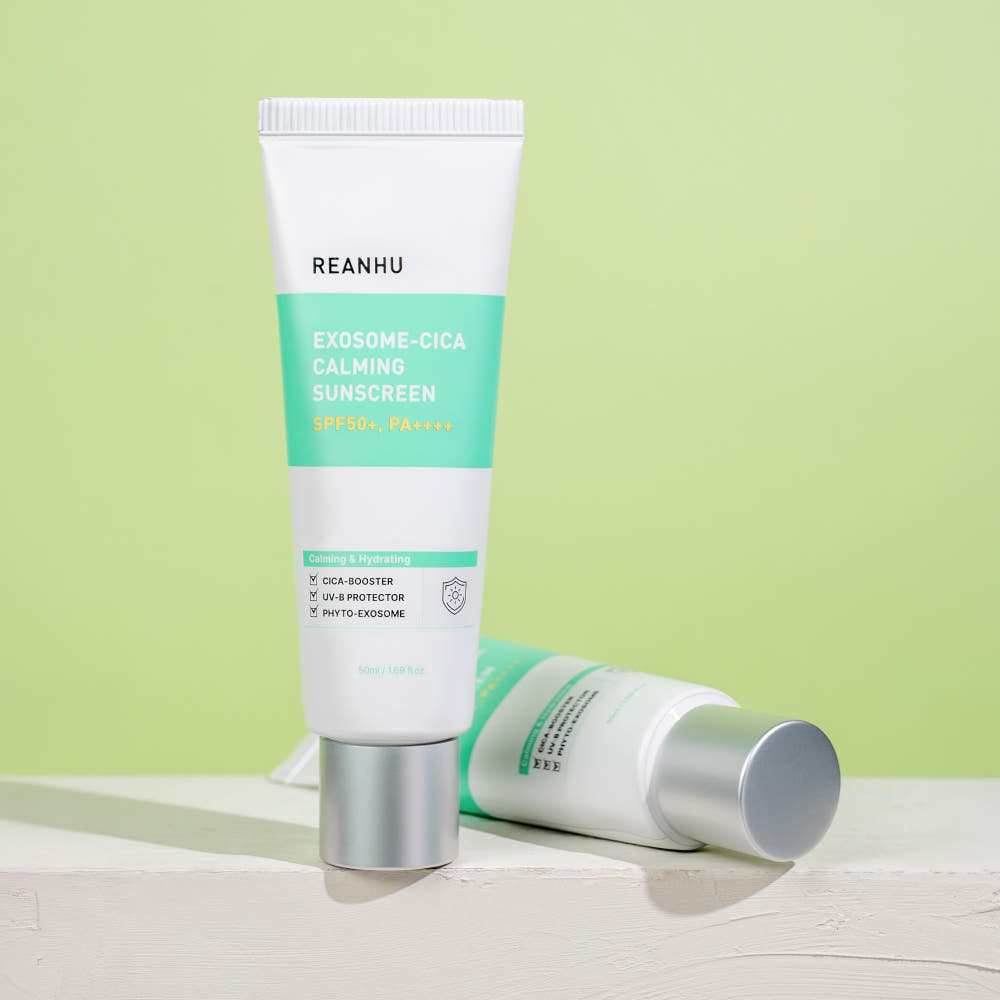 Décris l'image en français: REANHU Exosome Cica Calming Sunscreen 50ml, tube sur fond vert pastel, vue produit.