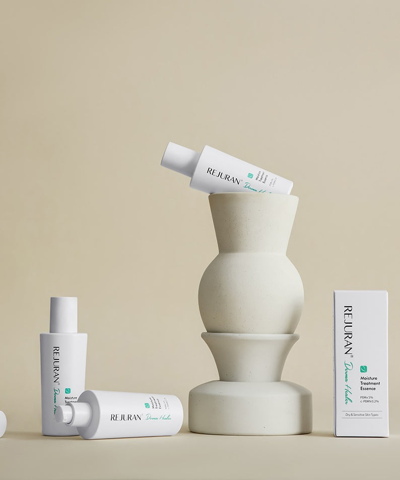 Décris l'image en français: REJURAN Derma Healer Moisture Treatment Essence 70g, flacon et boîte, studio beige minimaliste.