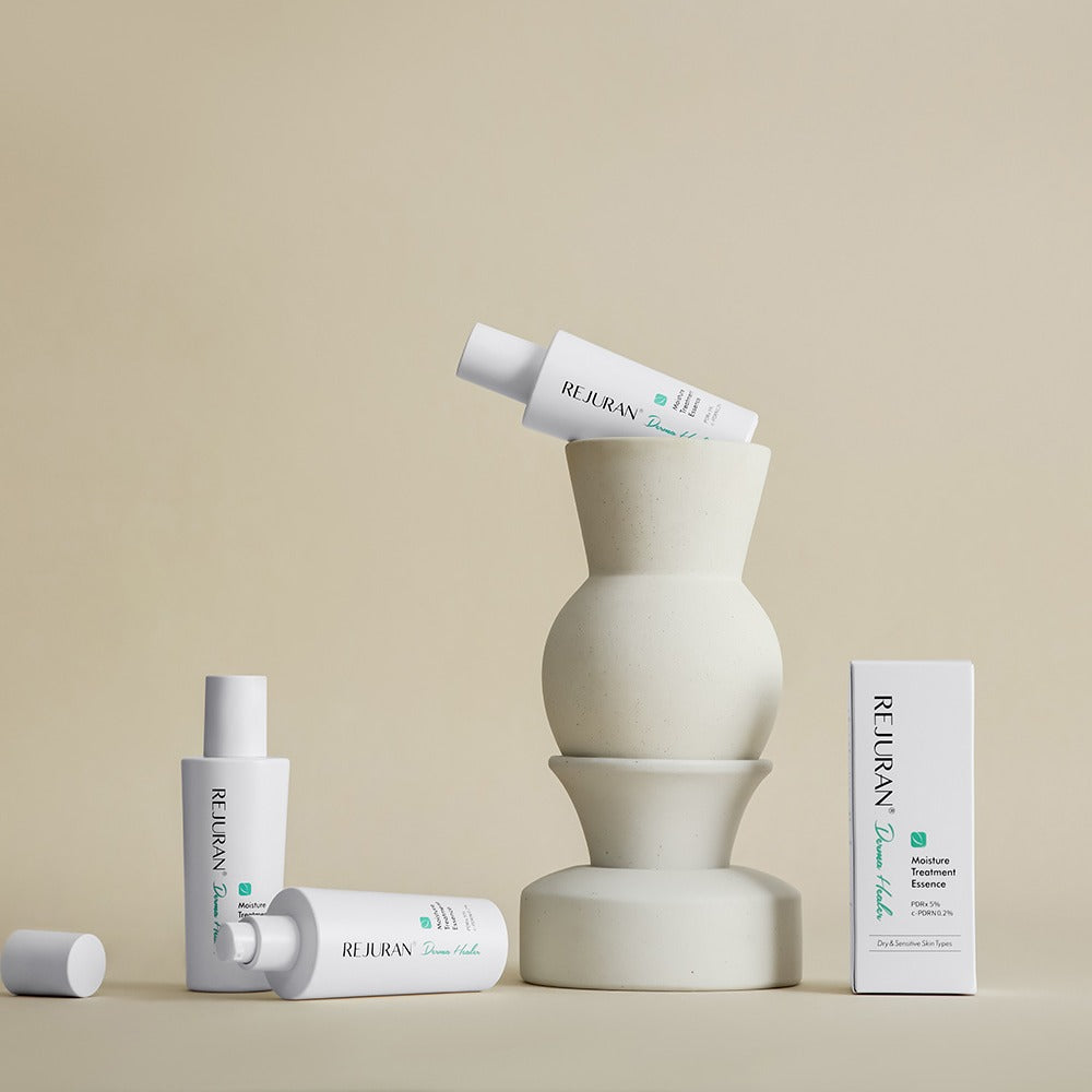 Décris l'image en français: REJURAN Derma Healer Moisture Treatment Essence 70g, flacon et boîte, studio beige minimaliste.