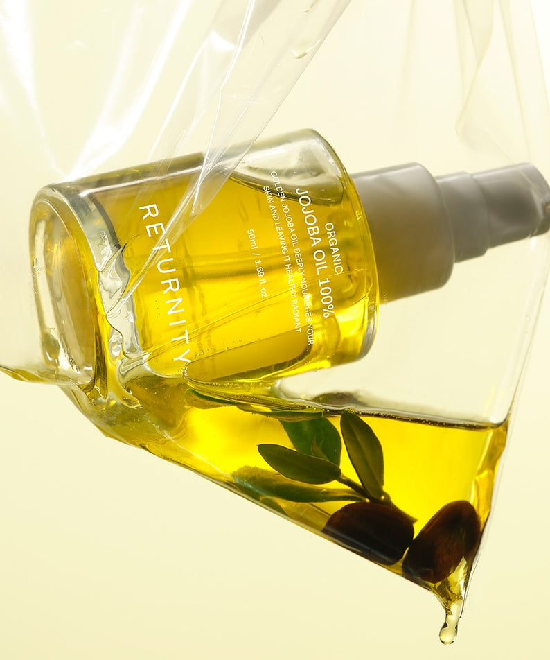 RETURNITY Organic Jojoba Oil 100% 50ml, flacon jaune et huile versée sur fond clair, avec feuilles de jojoba.