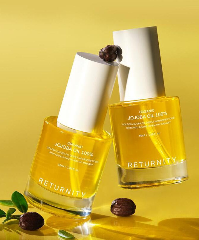 RETURNITY Organic Jojoba Oil 100% 50ml, flacons d’huile bio sur fond jaune ensoleillé, grains de café et feuilles vertes