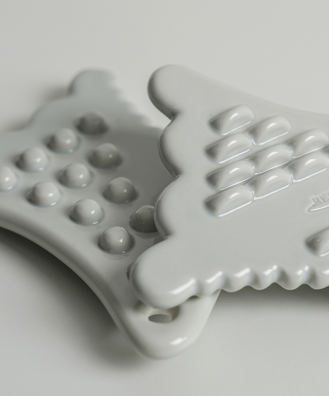 RETURNITY Mini Guasha en céramique blanche avec crêtes texturées pour massage, gros plan. Accessoire beauté pour soins du visage.