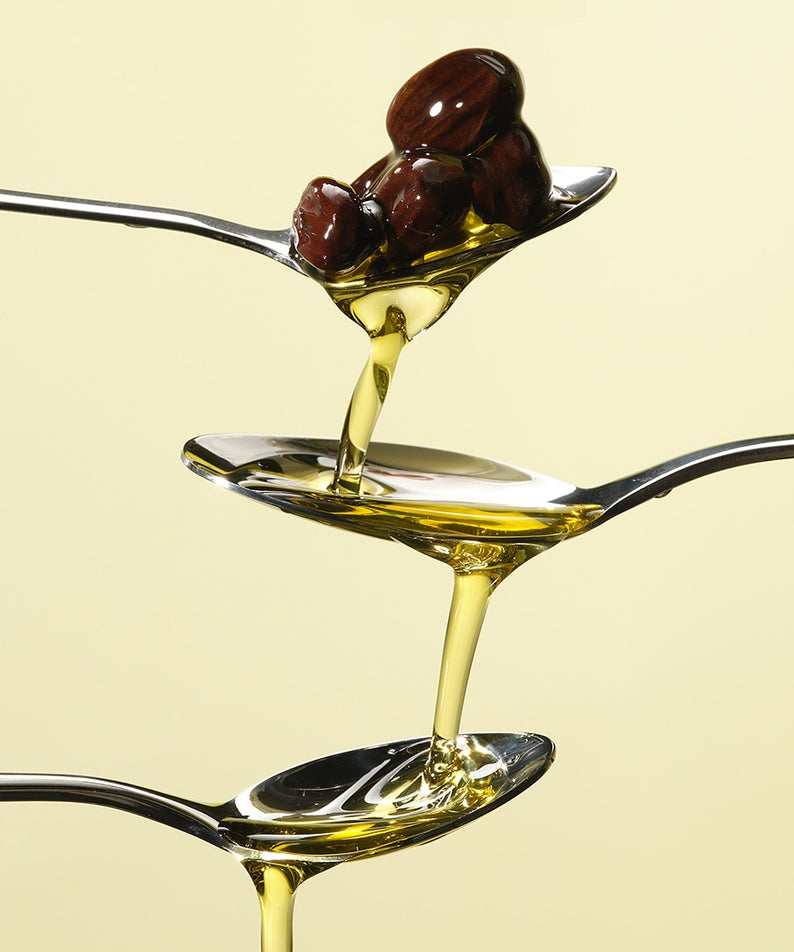 RETURNITY Organic Jojoba Oil 100% 50ml versé d'une cuillère à l'autre avec des graines.