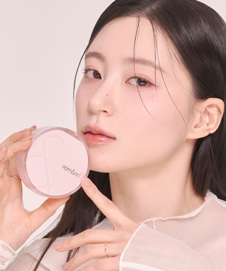 Femme tenant le ROMAND Bloom in Coverfit Cushion avec douceur. Maquillage léger et délicat. Photo produit cosmétique.