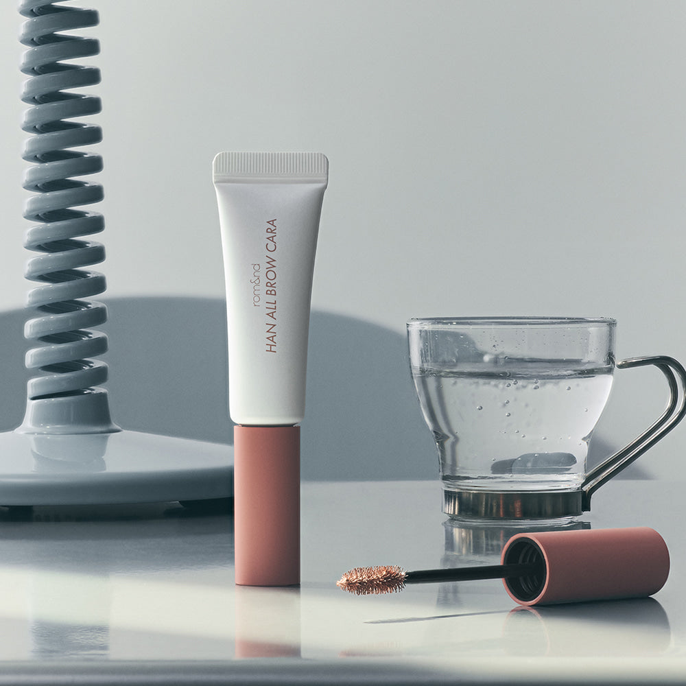 ROMAND  Hanol Brow Cara Single Item, tube maquillage sourcils ROMAND sur fond studio avec accessoires et miroir.