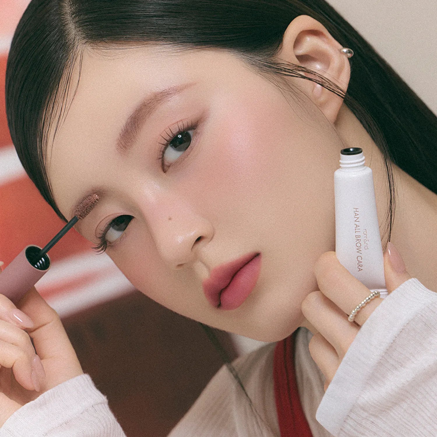 ROMAND  Hanol Brow Cara Single Item, maquillage sourcils sur modèle, tube en main, fond studio.