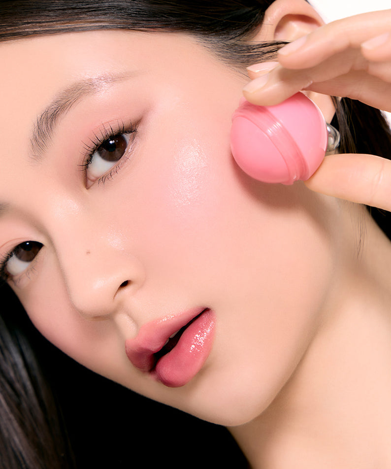 Maquillage avec ROMAND Juicy roll cheek, blush naturel et frais sur une joue avec applicateur rose. Beauté et élégance moderne.