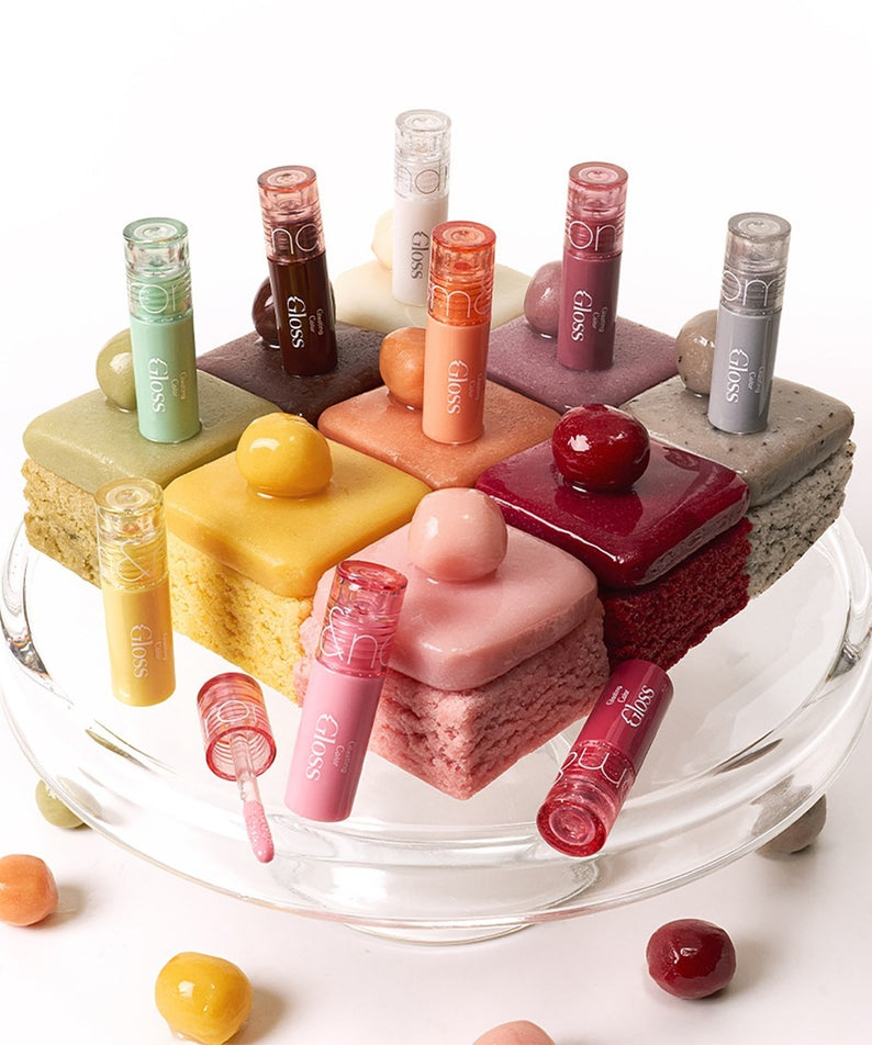 ROMAND MINI Glasting Color Gloss de la marque ROMAND, sur un plateau visuel avec mini gâteaux colorés.