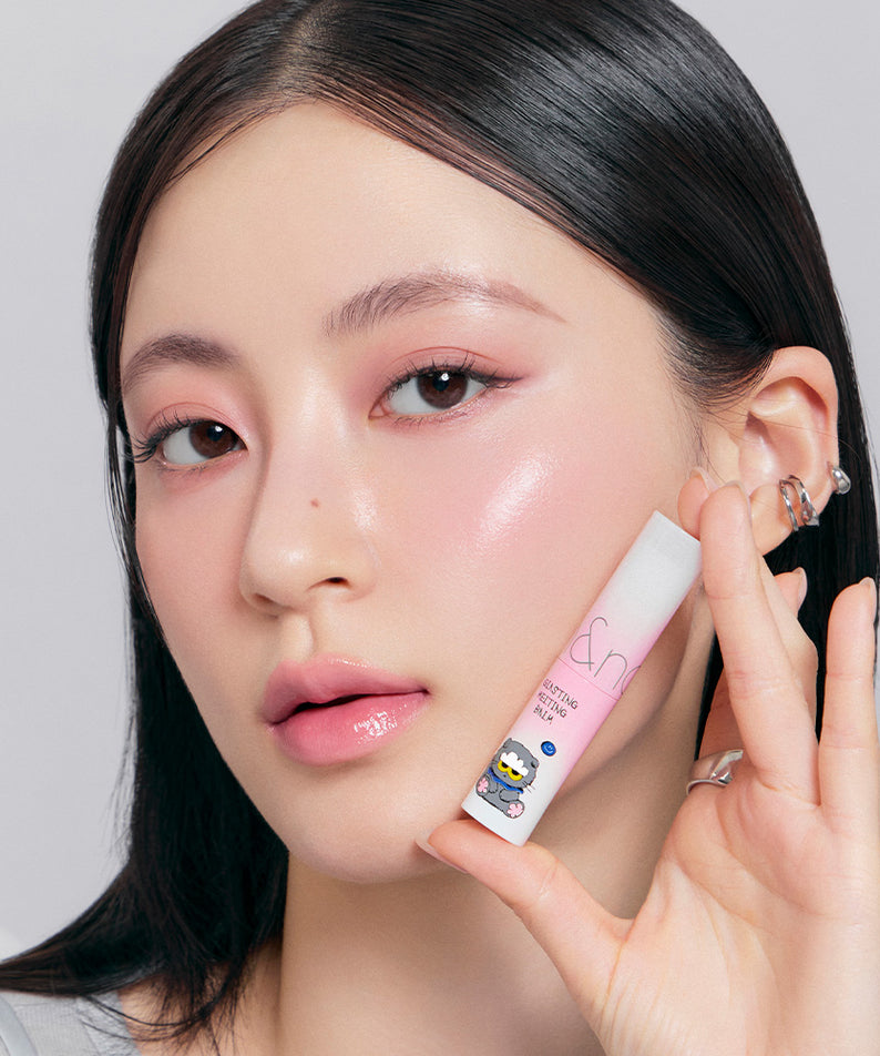ROMAND x Joanne Friends Glasting Melting Balm, tube sur la main, maquillage lumineux sur fond clair, collection ROMAND/Joanne