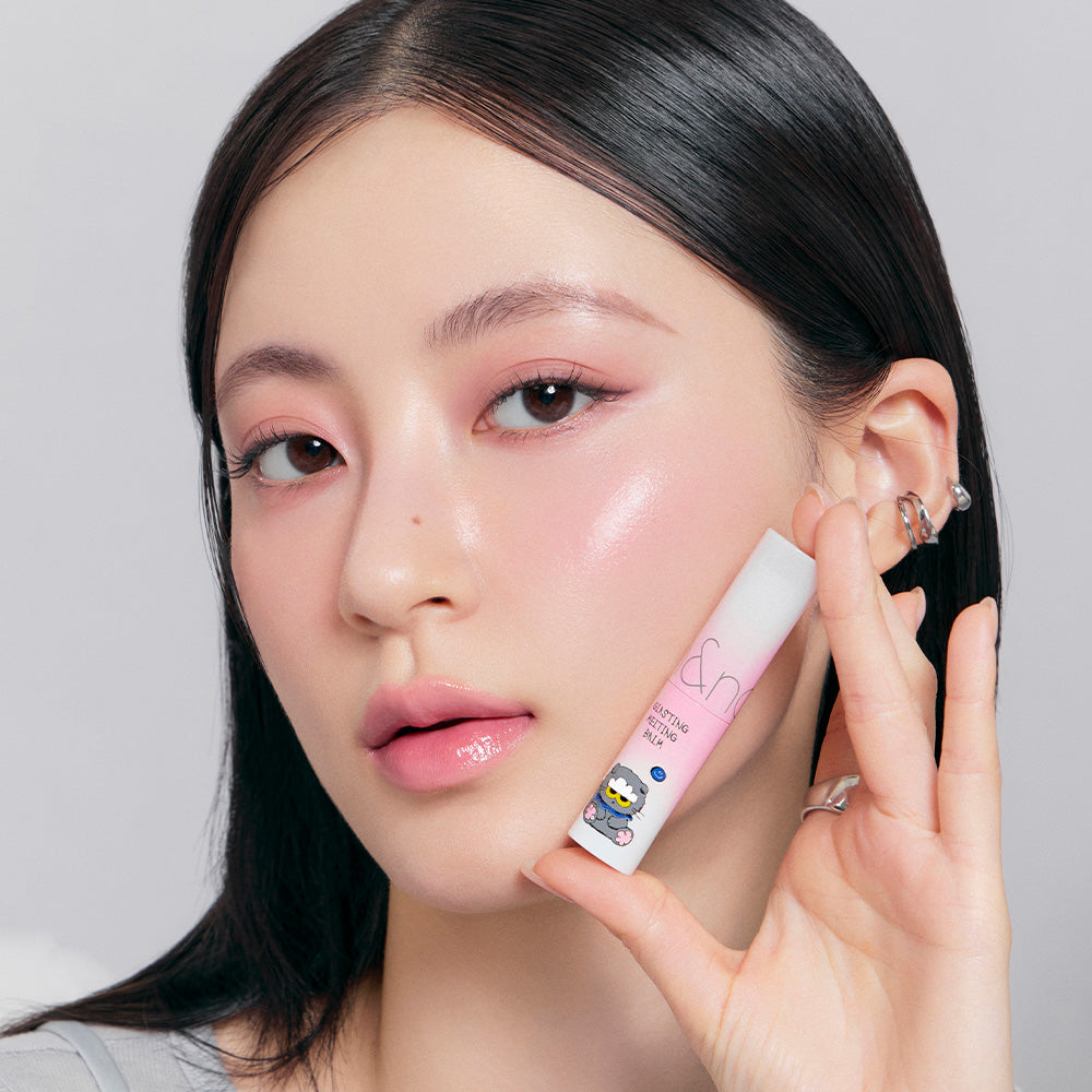 ROMAND x Joanne Friends Glasting Melting Balm, tube sur la main, maquillage lumineux sur fond clair, collection ROMAND/Joanne