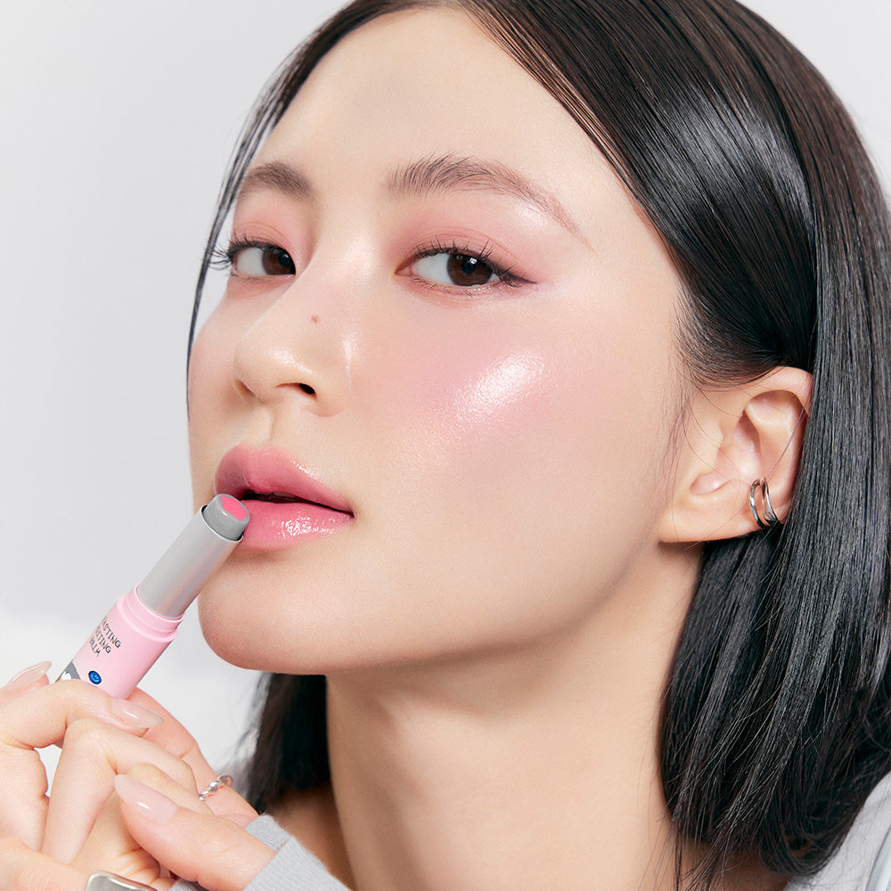 ROMAND x Joanne Friends Glasting Melting Balm, femme appliquant un baume rosé, maquillage glowy, packaging rose sur fond clair.