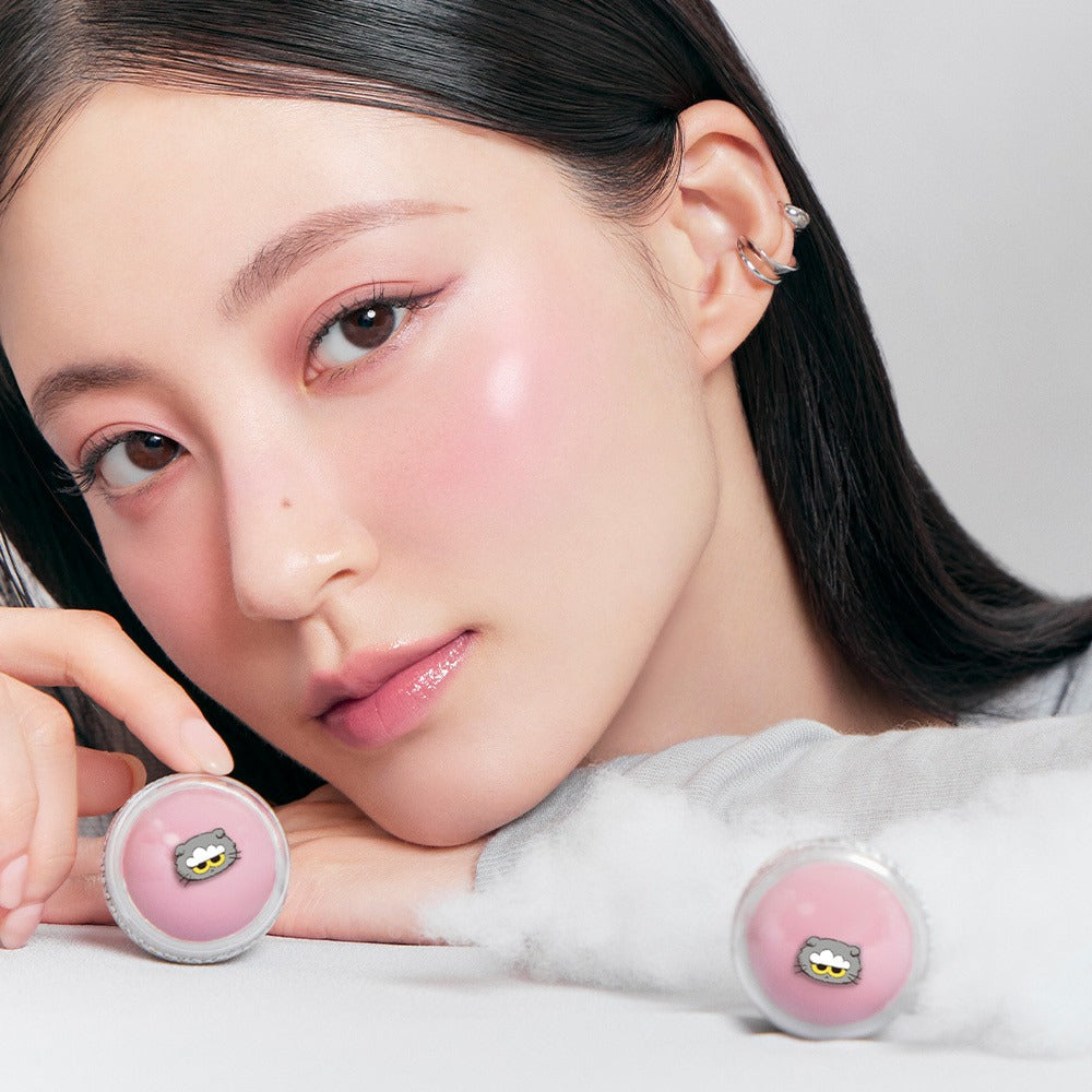 ROMAND x Joanne Friends Juicy R Cheek (Special Set) de ROMAND sur le visage d’une femme, avec poudres roses en décor.
