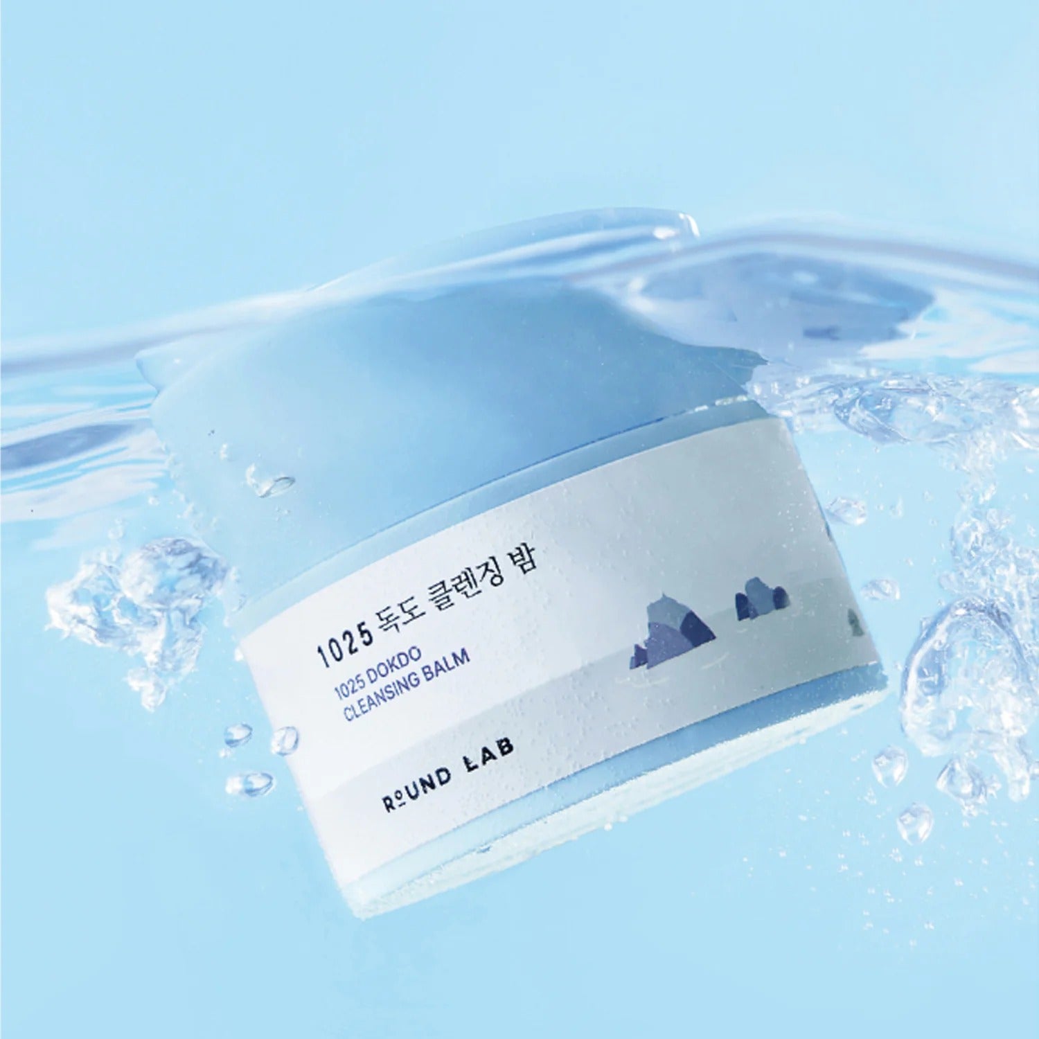 ROUND LAB 1025 Dokdo Cleansing Balm 50ml de ROUND LAB, posé dans des éclaboussures d’eau bleue.