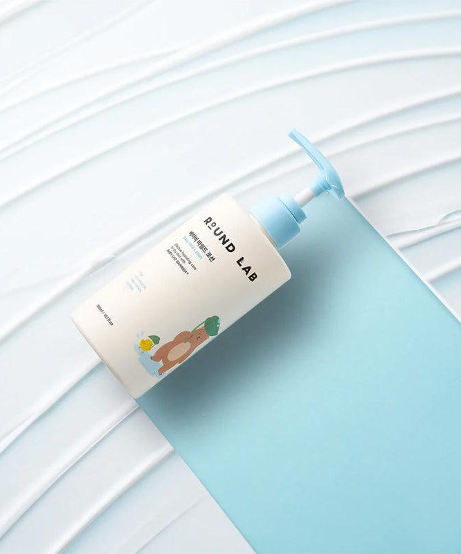 Bouteille de ROUND LAB Baby Mild Lotion 300ml sur fond bleu, soin doux pour la peau délicate des bébés.