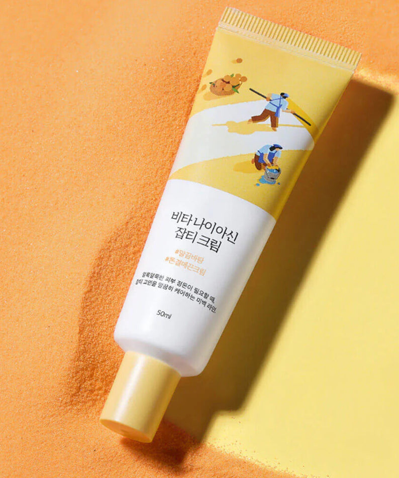 Crème anti-taches ROUND LAB Vita Niacin Spot Cream 50ml sur fond orange avec design moderne. Soin éclaircissant visage.