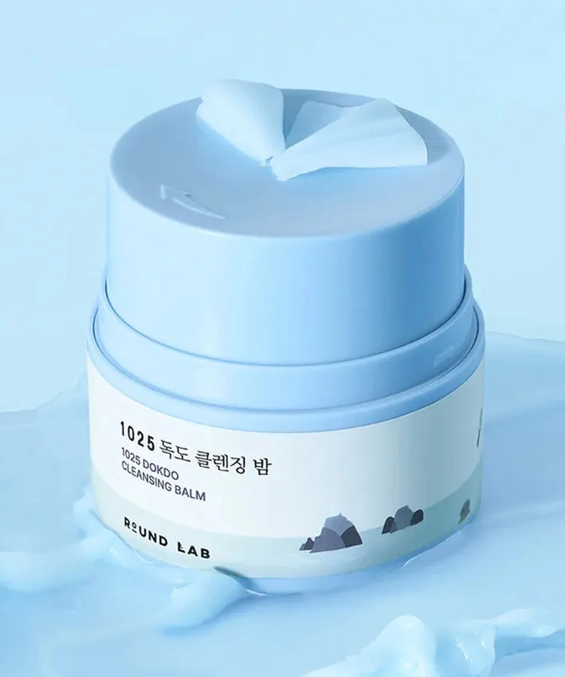 ROUND LAB 1025 Dokdo Cleansing Balm 50ml dans un pot bleu sur fond de liquide bleu, vue de près du produit de soin du visage.