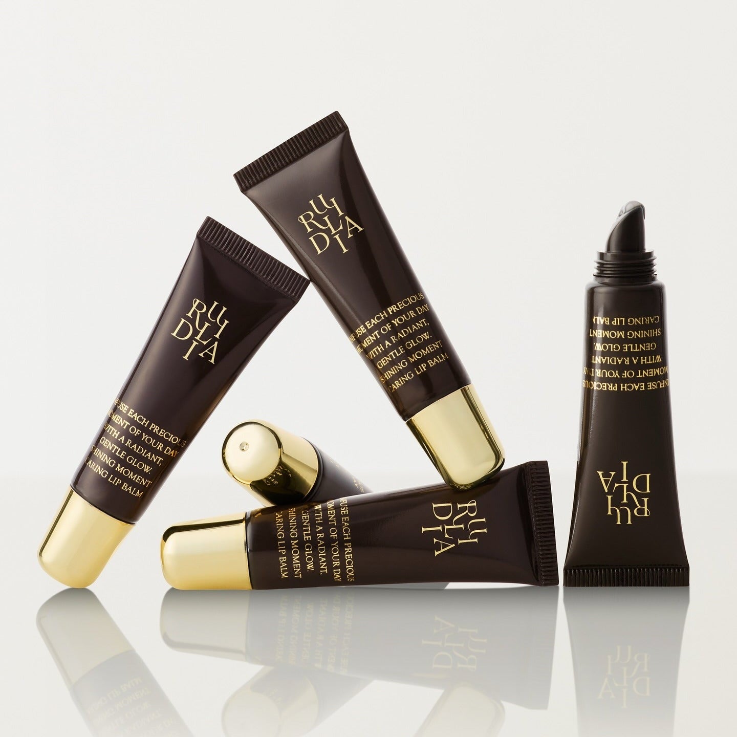 RULIDIA Shining Moment Caring Lip Balm 8g, tubes marron et or sur fond clair, marque RULIDIA, visuel promo.