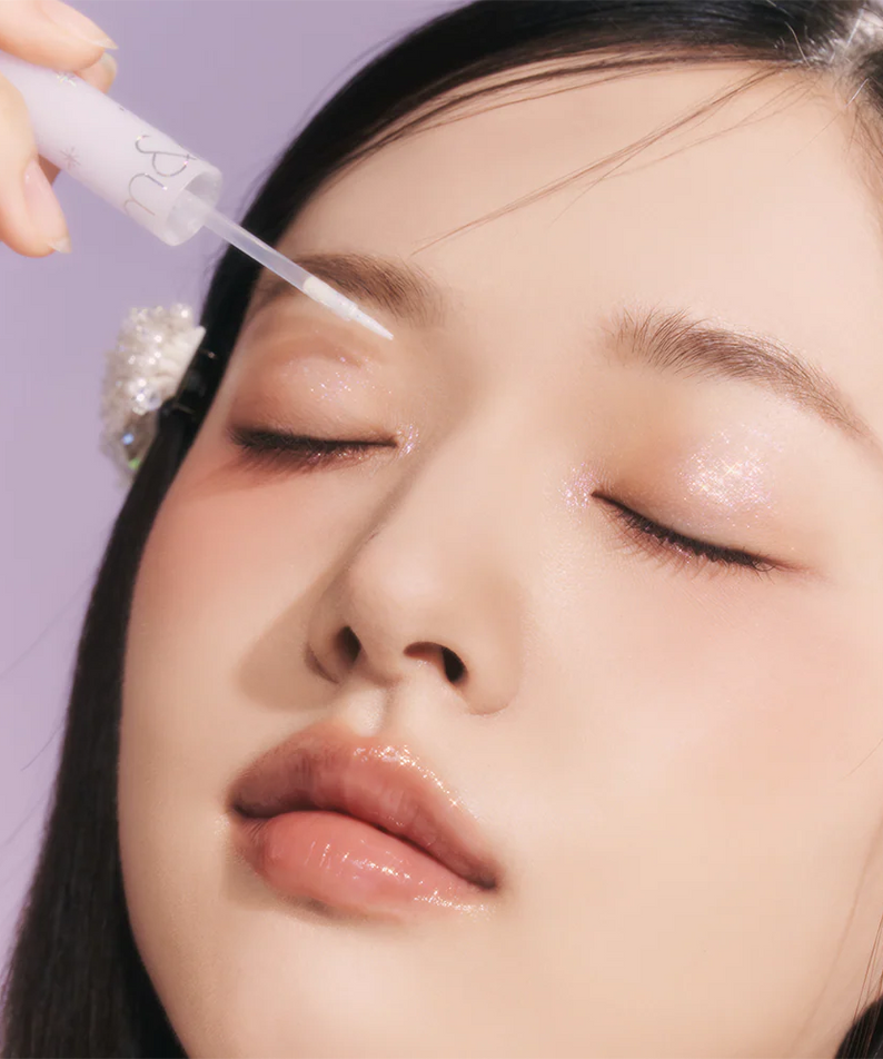 ROMAND The Universe Liquid Glitter, maquillage yeux pailletés sur visage, marque Romand en contexte violet, main appliquant