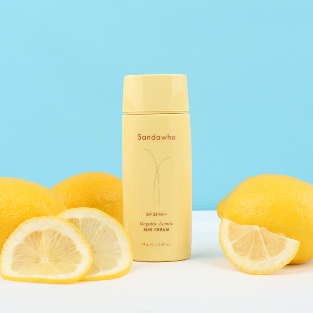 SANDAWHA Organic Lemon Sunscreen 70g, crème solaire bio au citron sur fond bleu avec citrons, marque sur le flacon.