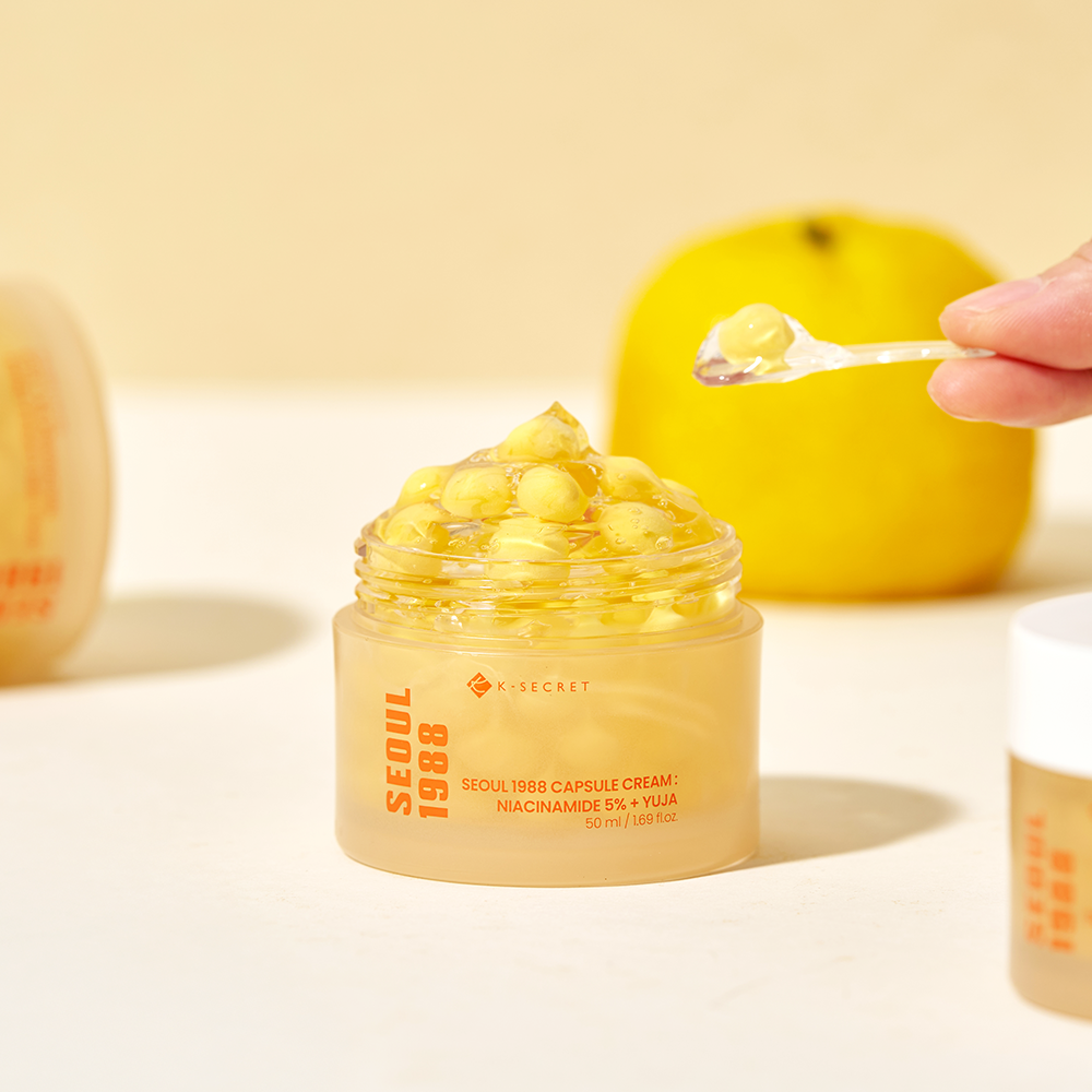 Décrivez l’image : pot de crème SEOUL 1988  Niacin Yuja Capsule Cream 50ml, marque sur packaging, crème dorée à la main