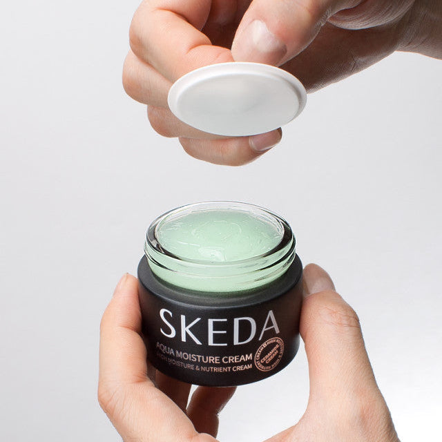 SKEDA Aqua Moisture Cream 50g de SKEDA : pot ouvert avec crème hydratante verte, mains en contexte cosmétique