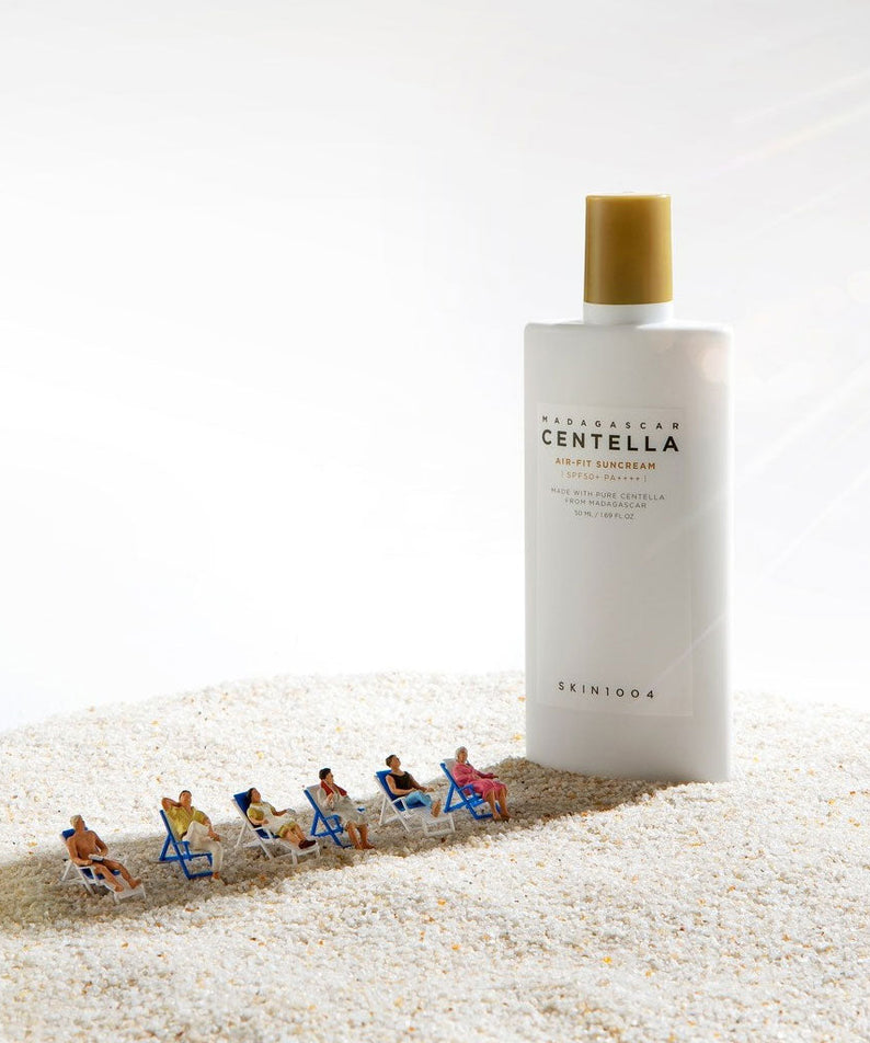 SKIN1004 Madagascar Centella Air-fit Sunscreen Plus 50ml, bouteille crème solaire sur sable blanc avec enfants au soleil.