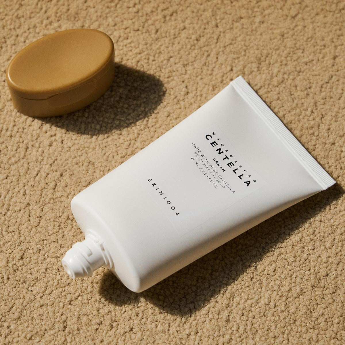SKIN1004 Madagascar Centella Cream 75ml, tube de crème et pot sur tapis beige, style skincare de la marque