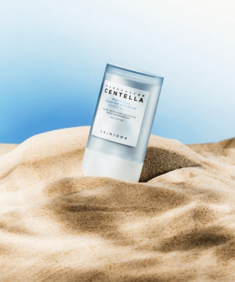 SKIN1004 Madagascar Centella Hyalu-Cica Silky Fit Sun Stick 20g de SKIN1004, sur tissu beige et fond bleu, en contexte soleil.
