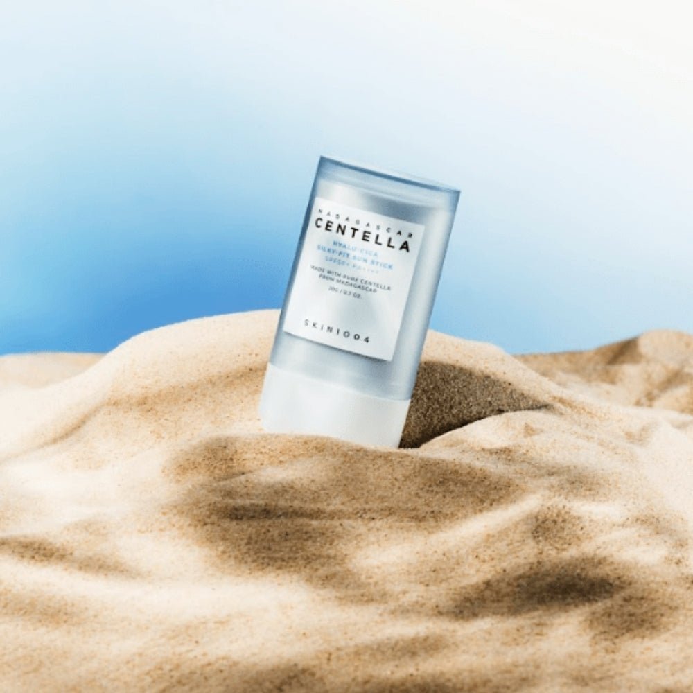 SKIN1004 Madagascar Centella Hyalu-Cica Silky Fit Sun Stick 20g de SKIN1004, sur tissu beige et fond bleu, en contexte soleil.
