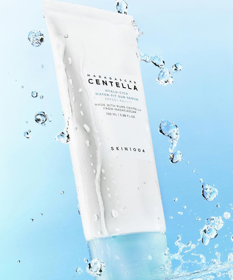 SKIN1004 Madagascar Centella Hyaluronic Acid Water-Fit Sun Serum 100ml, bouteille blanche sur fond bleu avec éclaboussures d'eau.
